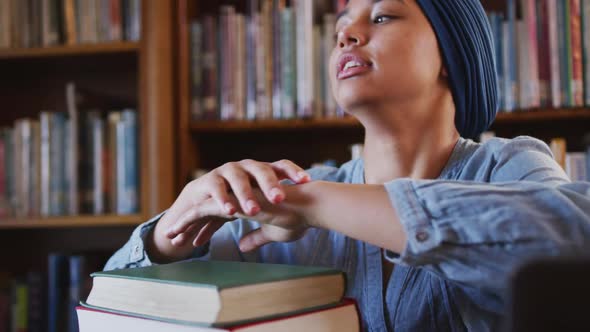 Asian female student wearing a blue hijab sitting and leaning on a pile of books and thinking