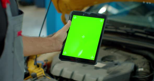 Car Service Manager or Mechanic Uses a Tablet Computer with a Green Screen Mock Up That Is Pointed