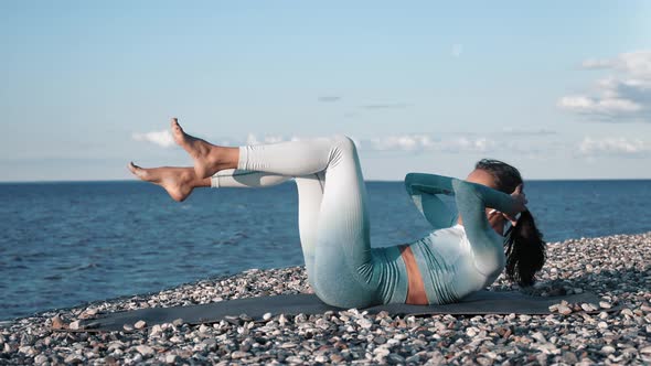 Brunette Sportswoman Training Abdominal Muscle Lying on Pebble Beach Sunset Coastline