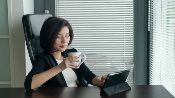 Business Woman Sitting Behind Desk in Office Using Tablet