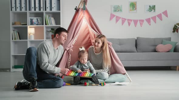 Portrait of Young Parents with Small Female Child Have Fun Playing Together on Background of Wigwam