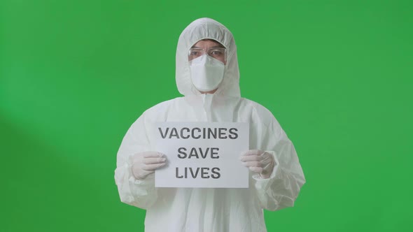 Asian Man Wear Protective Uniform PPE And Holding Vaccines Save Lives Sign In Green Screen Studio