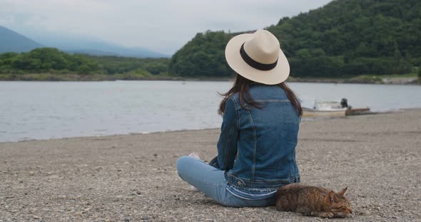 Woman sit at the lake side with a wild cat in shojiko of Japan