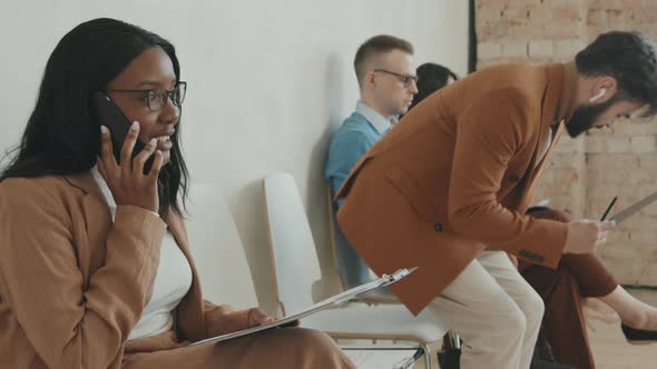 Black Woman Chatting on Phone in Queue for Job Interview