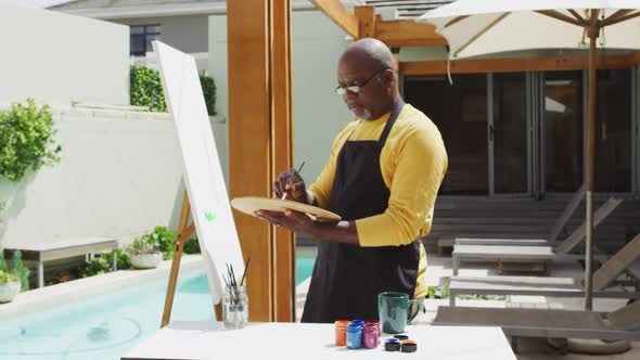 African american senior man standing on a terrace and painting