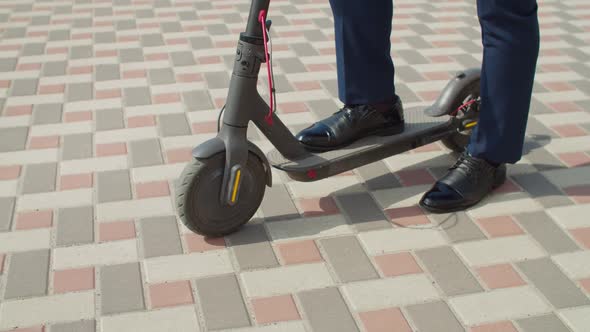 Businessman Standing on Electric Kick Scooter on Sidewalk