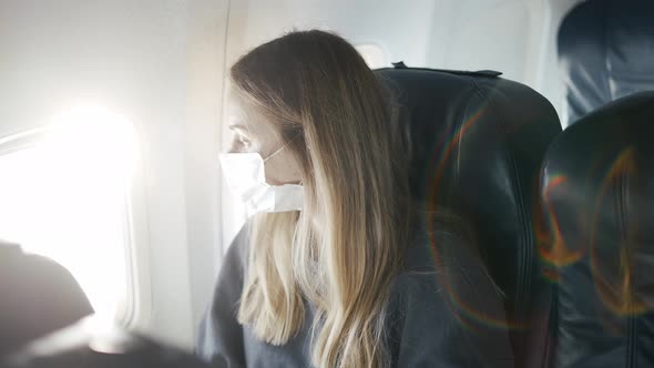 Woman in Protective Mask on Plane Looking to Window