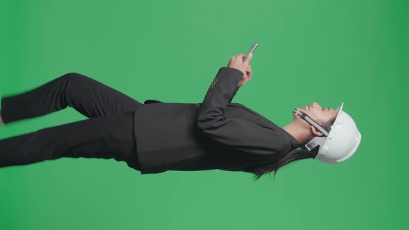 Side View Of Asian Female Engineer Looking Around While Using Smartphone And Walking On Green Screen