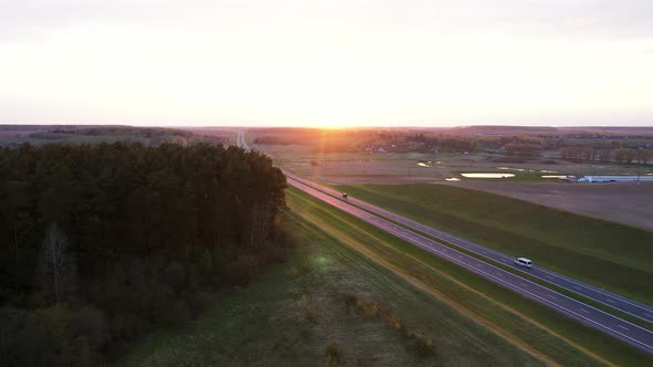 Aerial Over Intercity Distance Paved Highway Passing Through Fields At Sunset