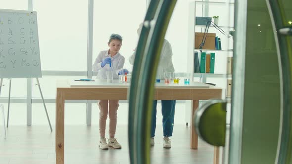 A Teenage Girl With a Teacher in Lab Coats andSafety GlassesConducts Experiments