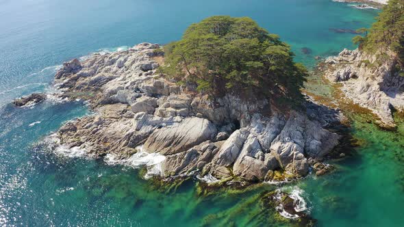 Rocky Island Washed By Waves Covered with Coniferous Trees in a Sea Bay