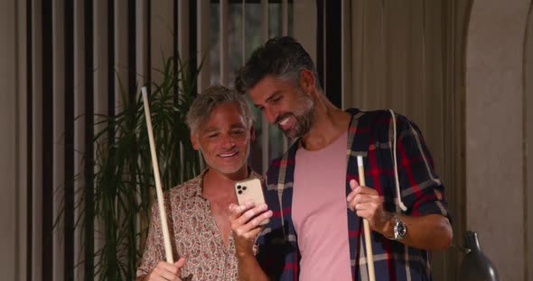 Cheerful men playing billiard while using mobile phone