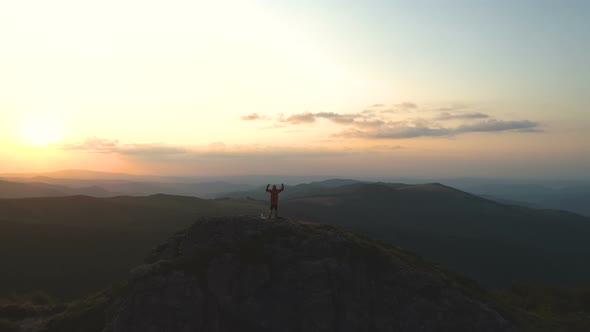 Young Hiker Reaches Mountain Top Outstretches Arms for Success with Beautiful Sunset Over Mountains