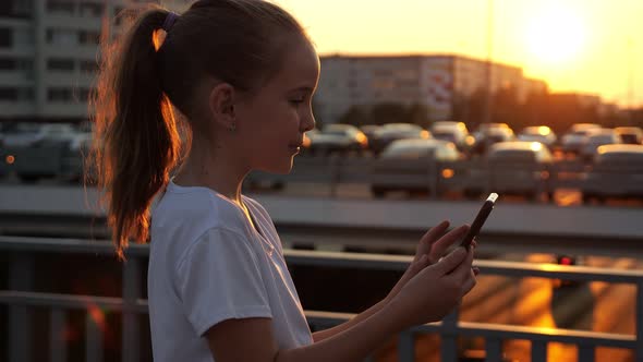 Girl Types on Smartphone and Poses for Selfie at Sunset