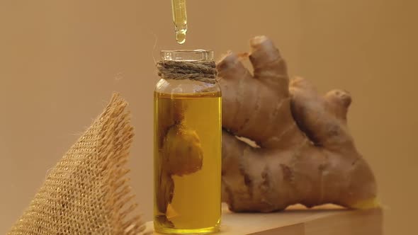 Glass Bottle of Essential Ginger Oil Dripping Ginger Root on Beige Background