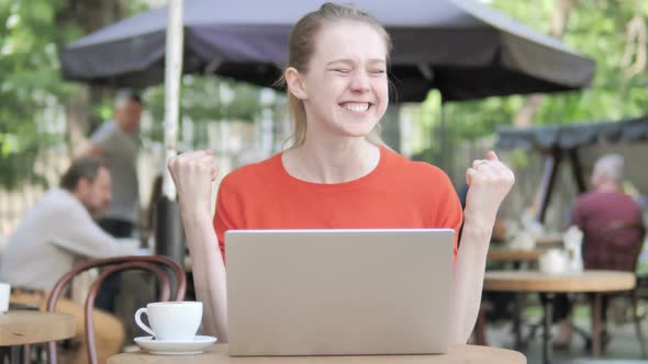 Young Woman Celebrating on Laptop Sitting in Cafe Terrace