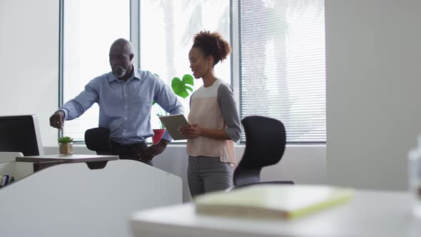 Diverse businessman and businesswoman talking, woman using digital tablet in office