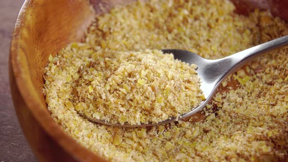 Full spoon of ground milled golden flaxseed in rustic wooden bowl. Macro