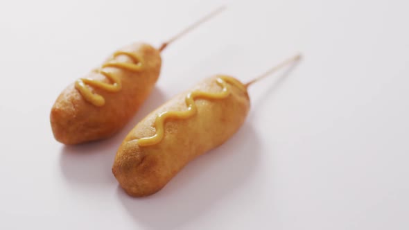 Video of corn dogs with mustard on a white surface