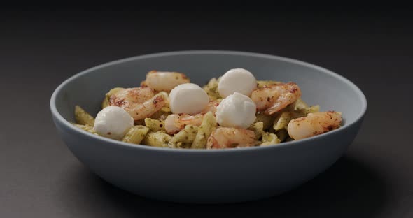 Slow Motion Add Mozzarella Balls to Pesto Penne with Shrimps in Blue Bowl on Black Background