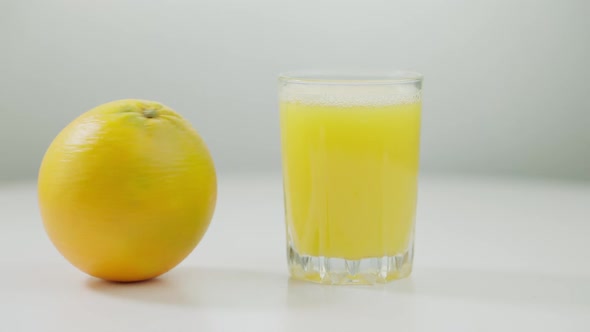 Closeup Orange Spinning on White Table with Glass of Juice Standing Aside