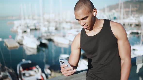Bald happy sportsman wearing black T-shirt typing on phone outdoors