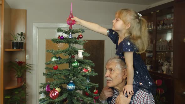 Little Child Girl and Senior Grandfather Decorating Artificial Christmas Tree at Home Slow Motion