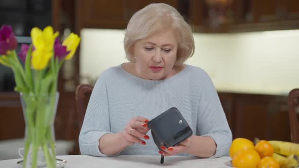 Poor Hopeless Senior Female Retiree Looking in Empty Wallet Sighing Shaking Head Looking at Camera