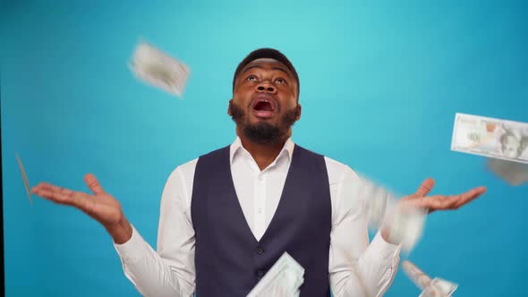 Young African American Businessman Standing Against Blue Background Dollar Banknotes Falling on Him