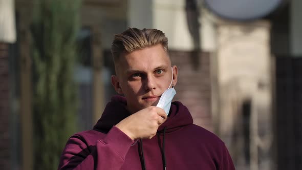 Portrait of a Young Man Looking at the Camera and Putting on a Medical Mask To Protect His Face From