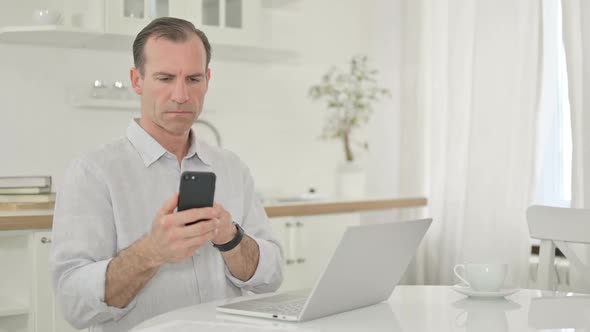 Professional Middle Aged Man Using Smartphone and Laptop at Home