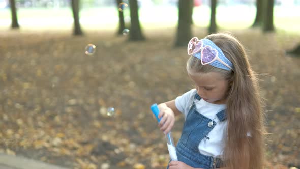 Little Happy Child Girl Blowing Soap Bubbles Outdoors in Summer Park