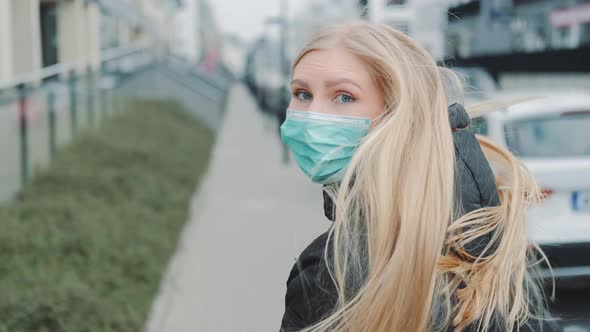 Young Blonde Woman in a Medical Mask Escaping From Somebody on the Street.