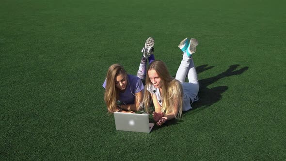 Two Girls Are Lying on the Lawn with Grass Using Laptop