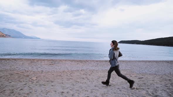 Happy and smiling young woman runs along the beach along the sea in spring time. Freedom concept