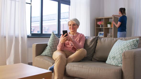 Old Woman with Smartphone and Housekeeper at Home