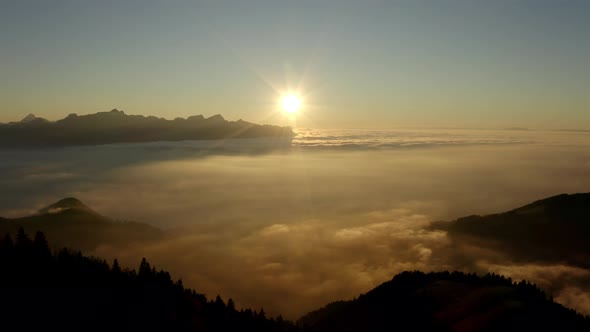 Descending alongside forest hill towards sea of clouds at sunset, the Alps in the background, Switze