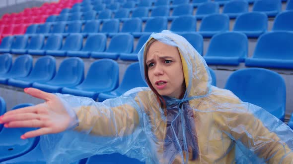 Unhappy Woman in Raincoat Sitting on Stadium Bleachers Alone Rooting for Favorite Sports Team