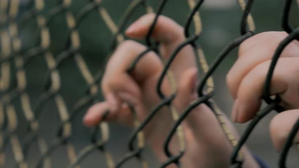 Closeup View of Young Woman's Hands Shaking Metal Mesh at Fenced Area