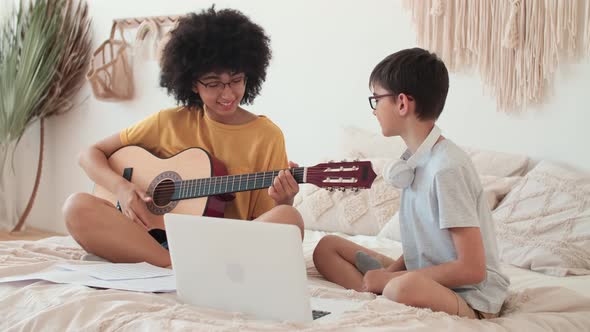 Cheerful Afro American Girl Guitarist and Boy Playing Guitar While Sitting on Bed