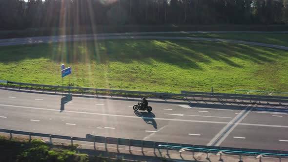 Man on Motorcycle Drives Through a Junction Sunset Time. Aerial Tracking Dron Shot. .