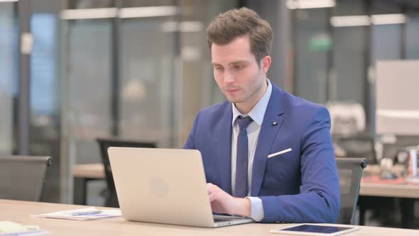 Businessman Smiling at Camera While Using Laptop in Office