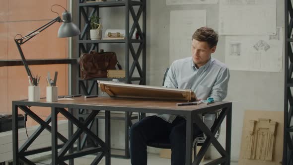 Architect Man Sits at Drafting Table in Modern Industrial Office During the Day