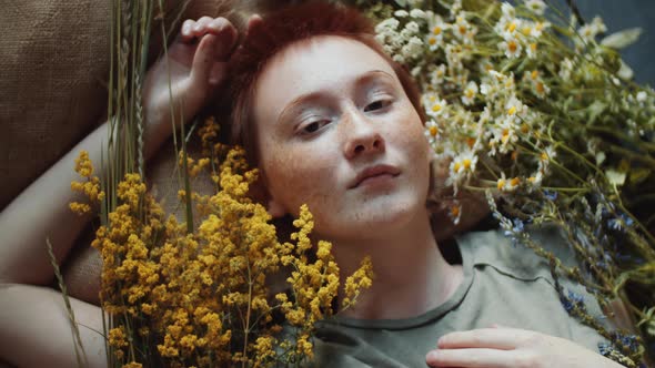 Redheaded Woman Lying among Meadow Flowers and Posing for Camera