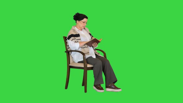 Friendly Senior Woman Sitting in Chair Reading a Book on a Green Screen Chroma Key