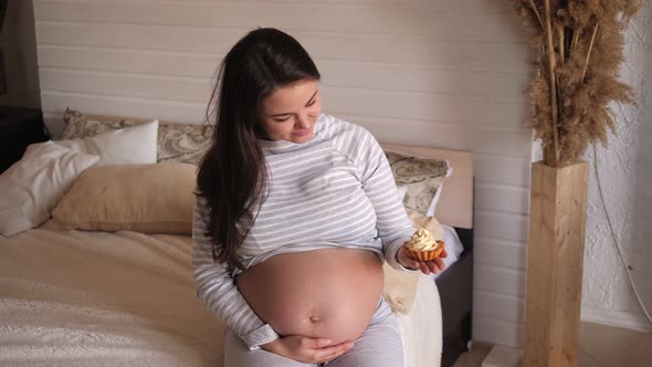 Portrait of a Happy Pregnant Girl with a Cake in Her Hands at Home on the Bed