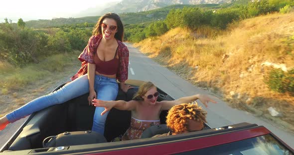 Beautiful young brunette sitting on hood of convertible car riding with friends