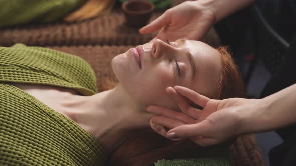 Young Caucasian Woman Receives a Facial Massage with Aromatic Essential Oil for Skin Care From a