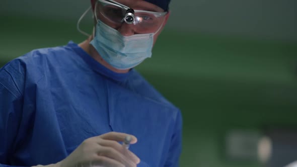 Young Caucasian Man in Uniform Cutting Dissection on Face of Unrecognizable Patient in Surgery Room