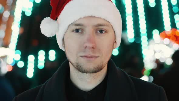 Serious Man Portrait with New Year Hat Looking at Camera, Bokeh of Christmas Garland Lights